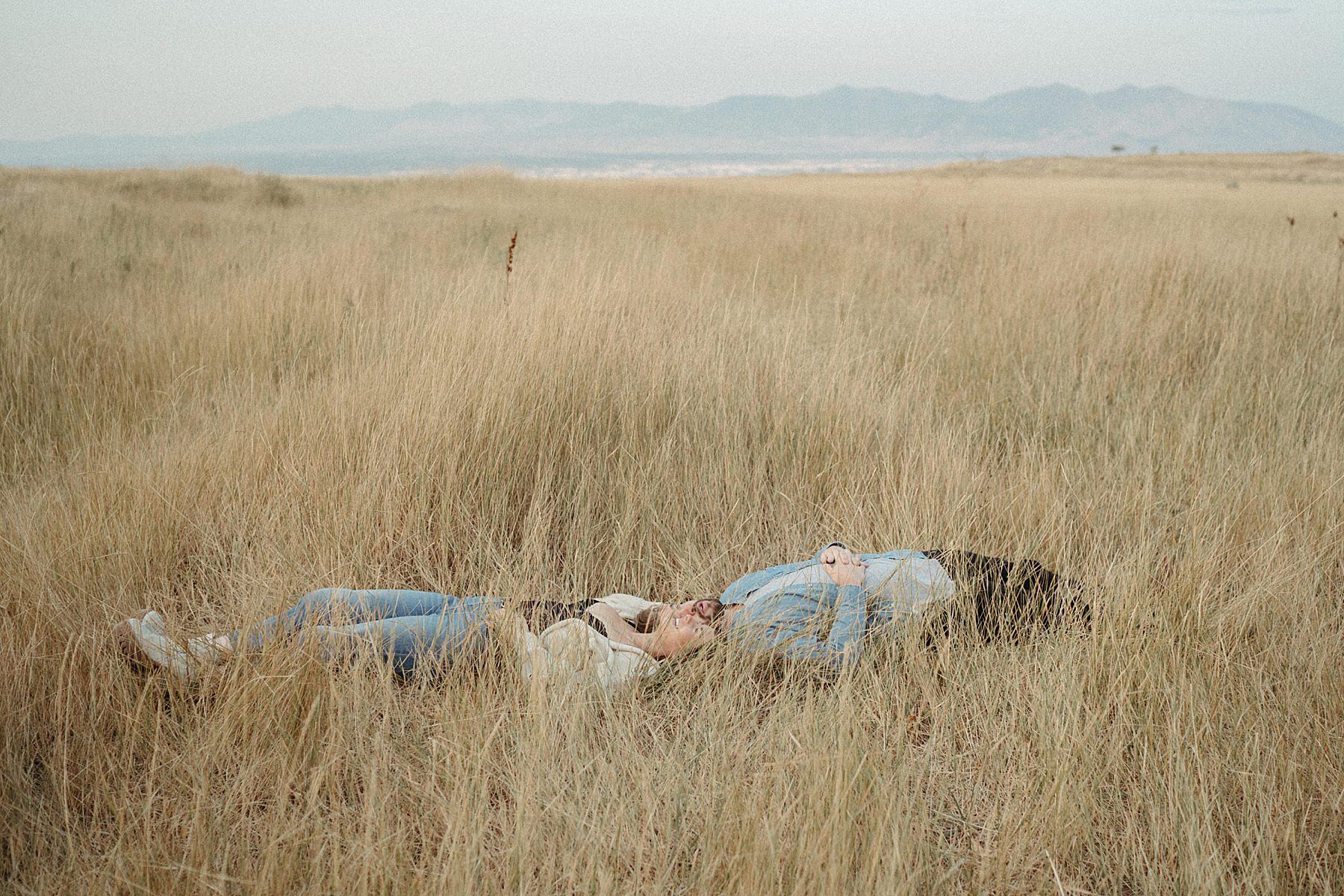 Utah Engagement photography, couple laying the the tall grass, mountain in the background